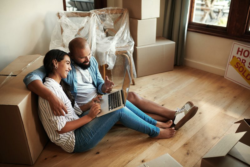 7ReasonstheBestBudgetAppforCouplesisSimplyGoogleSheets2 d24aa1a70636617831969d60004fc0f1 800 Shot of a young smiling couple sitting on the floor surrounded by moving boxes while they use a laptop